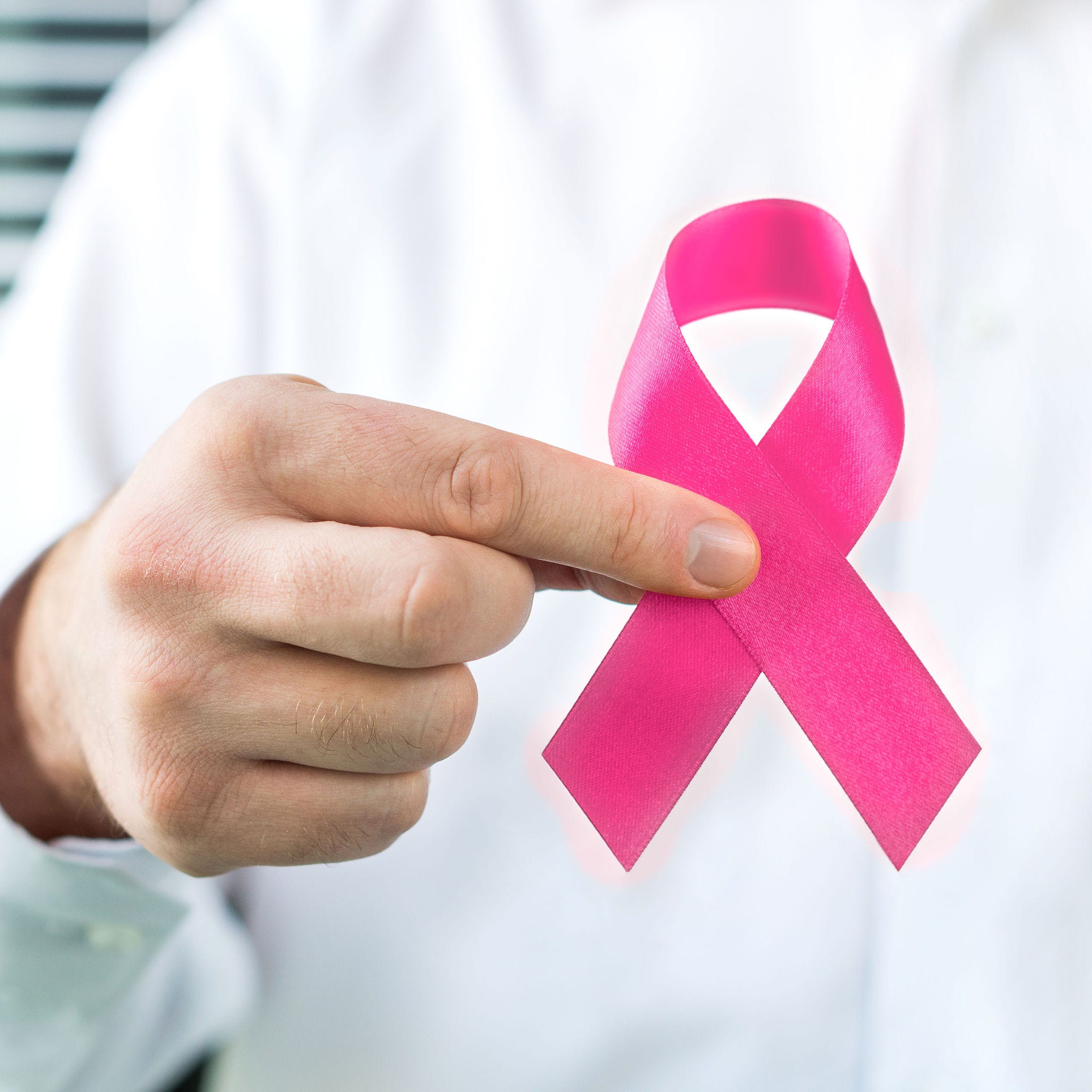 Hand holding pink ribbon to represent awareness of women's cancer